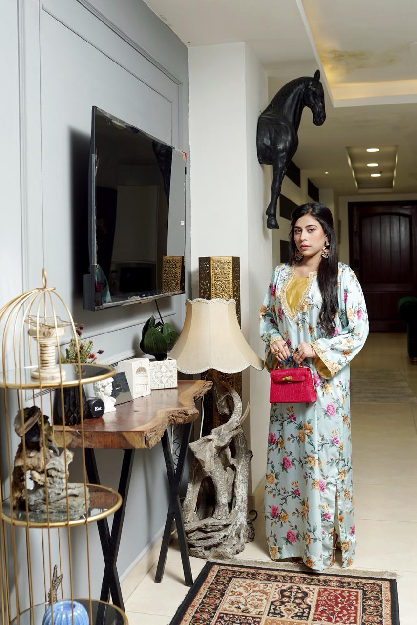 Woman in a floral dress standing in a stylishly decorated room with a TV and decorative items.