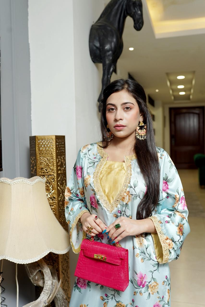 Woman in a floral dress holding a pink handbag in an indoor setting.